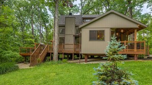A cabin with a deck, a staircase, and a small tree in the front yard.