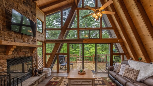 A spacious loft with a stone fireplace, a large wooden ceiling fan, and a cozy seating area with a leather couch and a coffee table.