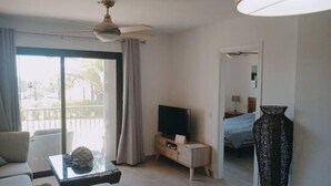 Et hotelværelse med balkon, et fjernsyn på et træstel, en stor vase og en seng med blåt sengetæppe.