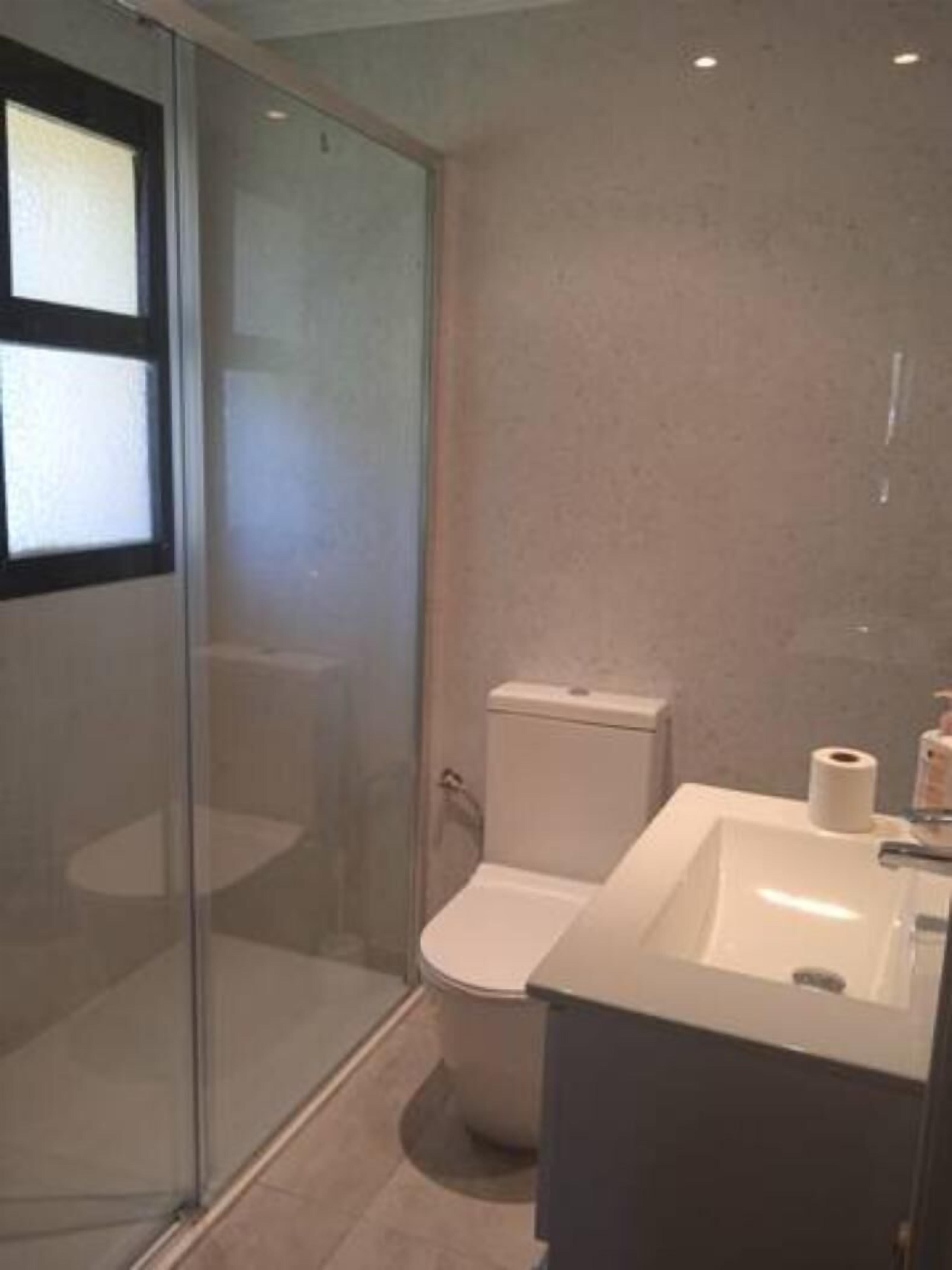 Ein modernes Badezimmer mit einer Duschkabine aus Glas, einer weißen Toilette und einem großen Waschbecken mit Spiegel.