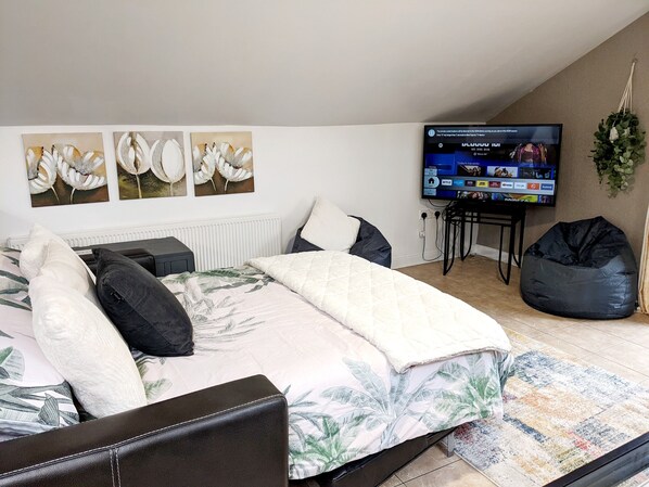 A bedroom with a bed, a TV, a bean bag, and wall art.