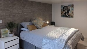 A modern bedroom with a bed, nightstands, a wall-mounted light, a framed picture, and a potted plant.