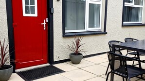 A red door with a small window, a black-framed window, and a potted plant.