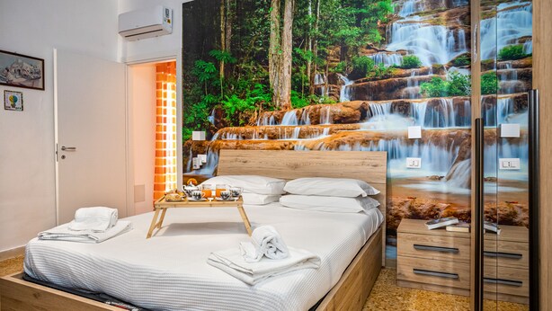 A neatly made bed with white linens, a tray with breakfast items, and a large mural of a waterfall on the wall.