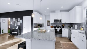A modern kitchen with white cabinets, granite countertops, stainless steel appliances, and pendant lighting.