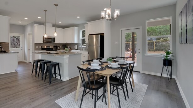 A modern kitchen with a central island, stainless steel appliances, pendant lighting, and a dining area with a round table and chairs.