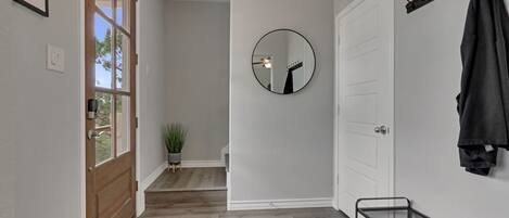 A hallway with a wooden door, a mirror, a coat rack, and a small plant.