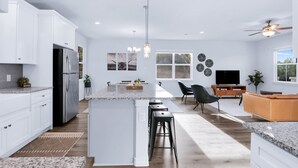 A modern kitchen with white cabinets, a stainless steel refrigerator, a granite countertop, and a central island with bar stools.