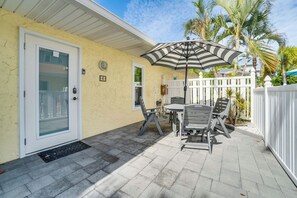 A patio with a table and chairs, a striped umbrella, and a white fence.