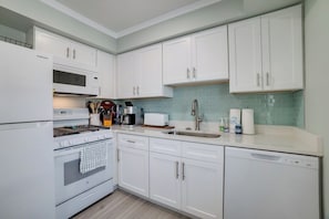 A modern kitchen with white cabinetry, a built-in microwave, a stove, a dishwasher, and a sink.