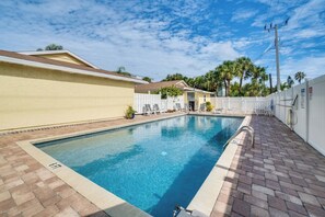 A rectangular swimming pool with a brick border, surrounded by a white fence and a paved walkway.