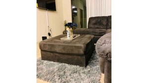 Un salon avec un tapis gris à longues mèches, un pouf marron et un canapé brun foncé.