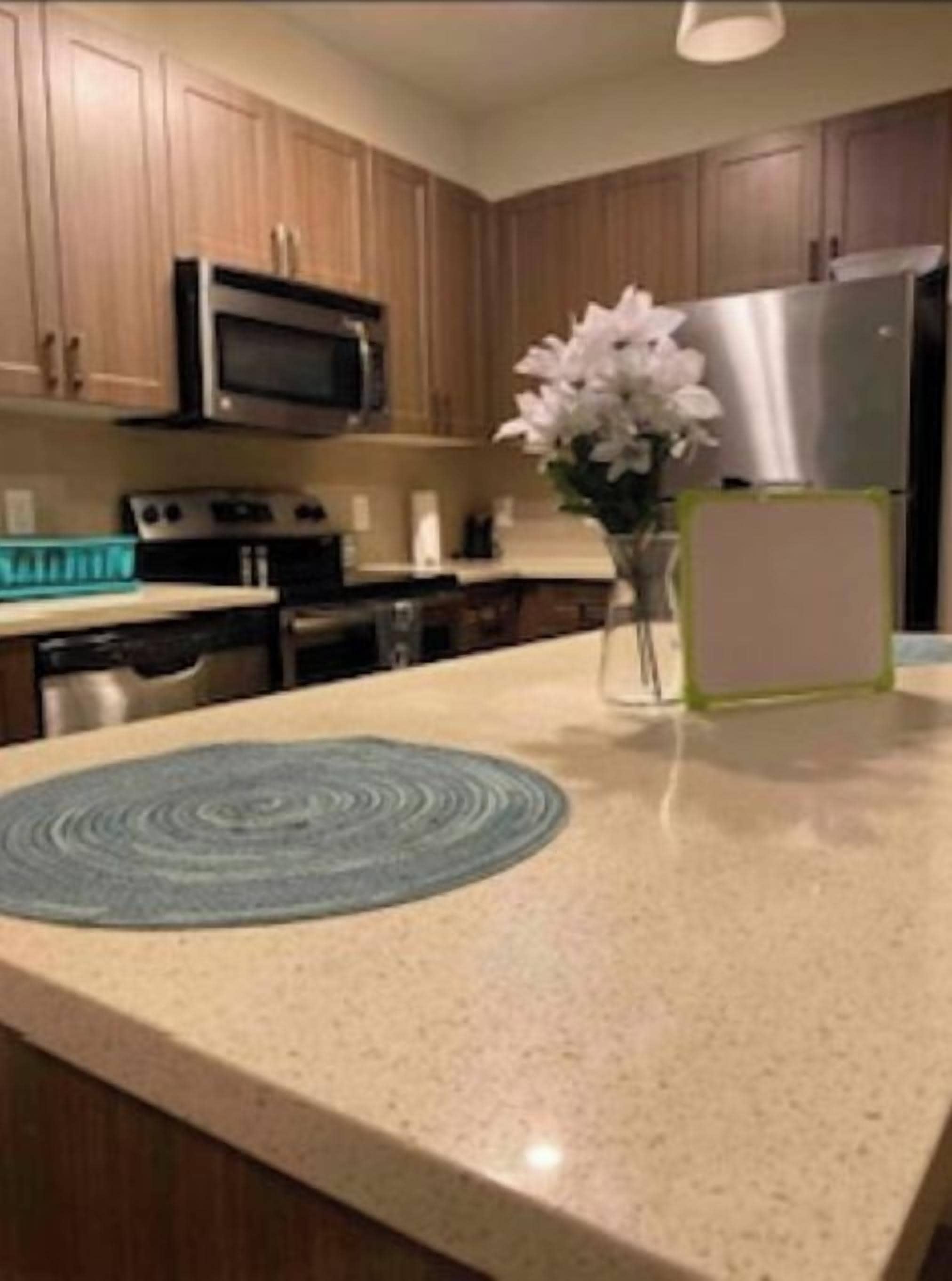 Une cuisine avec des meubles de rangement en bois, un four à micro-ondes, un réfrigérateur et un vase rempli de fleurs posé sur le plan de travail.