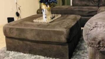 A living room with a grey shaggy carpet, a brown ottoman, and a dark brown sofa.