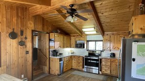 A wooden cabin kitchen with a ceiling fan, wooden cabinets, a stainless steel refrigerator, and a double oven.