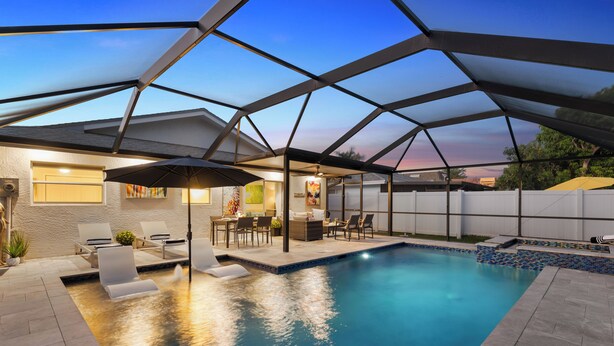 Piscina con un área de patio techada, sillas de descanso y una mesa con sombrillas.