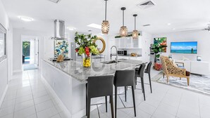 Una cocina moderna con una isla central, taburetes de bar, iluminación colgante y vistas al océano a través de un ventanal grande.