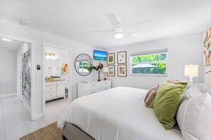 Un dormitorio moderno con una cama grande, un ventilador de techo, un televisor y obras de arte en las paredes.