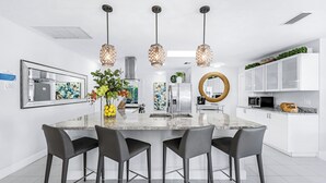 Una cocina moderna con una isla central, taburetes de bar, iluminación colgante y armarios blancos.