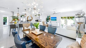 Una cocina moderna con armarios blancos, un comedor con mesa de madera y una sala de estar con sofá y televisor.