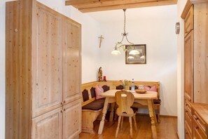 A wooden dining area with a bench, a table, and a hanging light fixture. - Zugspitzblick Apartment with Mountain Views, Garden, and Wi-Fi (Grainau)
