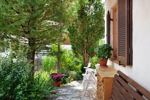 A stone pathway leading to a white bench and table set against a white wall with brown shutters. - Zugspitzblick Apartment with Mountain Views, Garden, and Wi-Fi (Grainau)