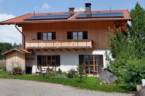 A wooden house with a balcony, solar panels on the roof, and a garden with a rock. - Zugspitzblick Apartment with Mountain Views, Garden, and Wi-Fi (Grainau)