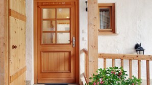 Una porta in legno con pannelli di vetro, una piccola finestra con tenda e una ringhiera in legno.