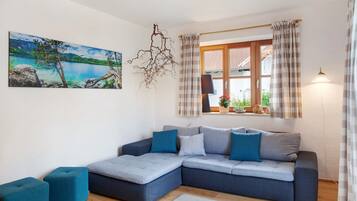 A modern living room with a sectional sofa, a painting of a lake, and a window with curtains.