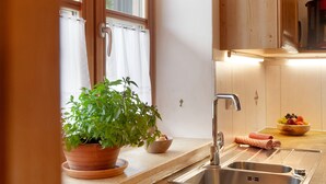 Una cucina con lavello, una pianta in vaso, una ciotola di frutta e pensili in legno.
