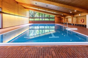 Una piscina con travi in legno, pavimento in mattoni e ampie finestre.