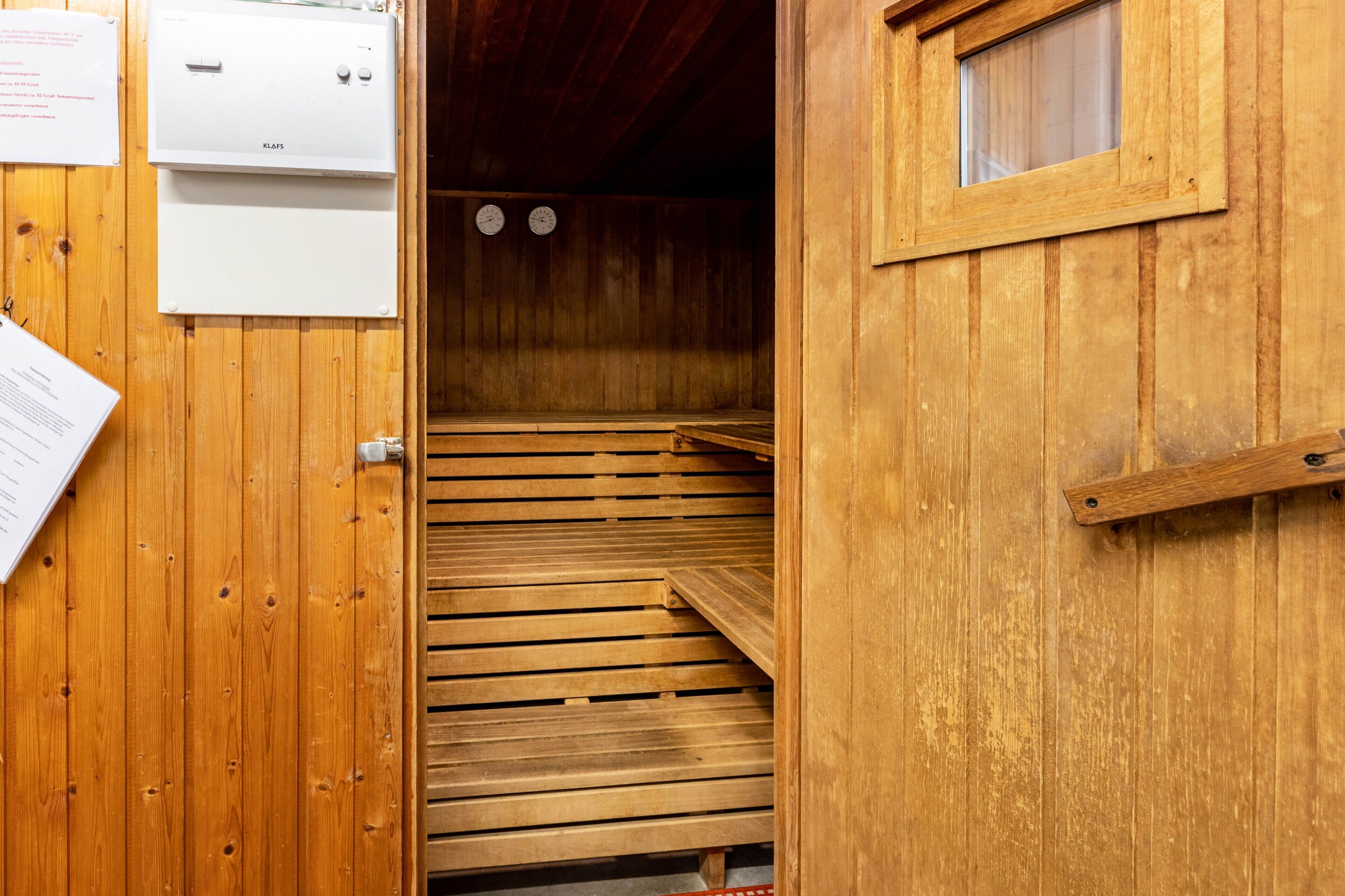 A wooden sauna with a wooden bench, a window, and a door.