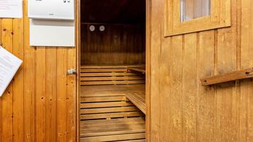 A wooden sauna with a wooden bench, a window, and a door.