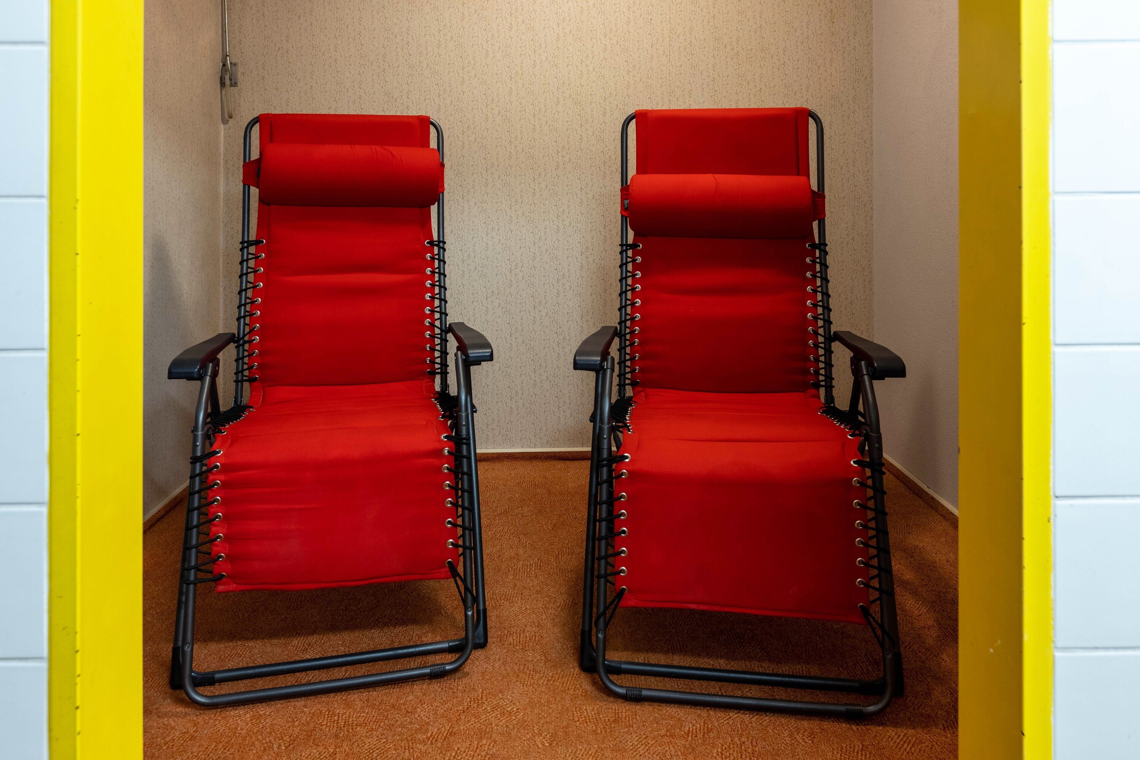 Deux chaises rouges à armature noire, dans une pièce aux murs jaunes et blancs.