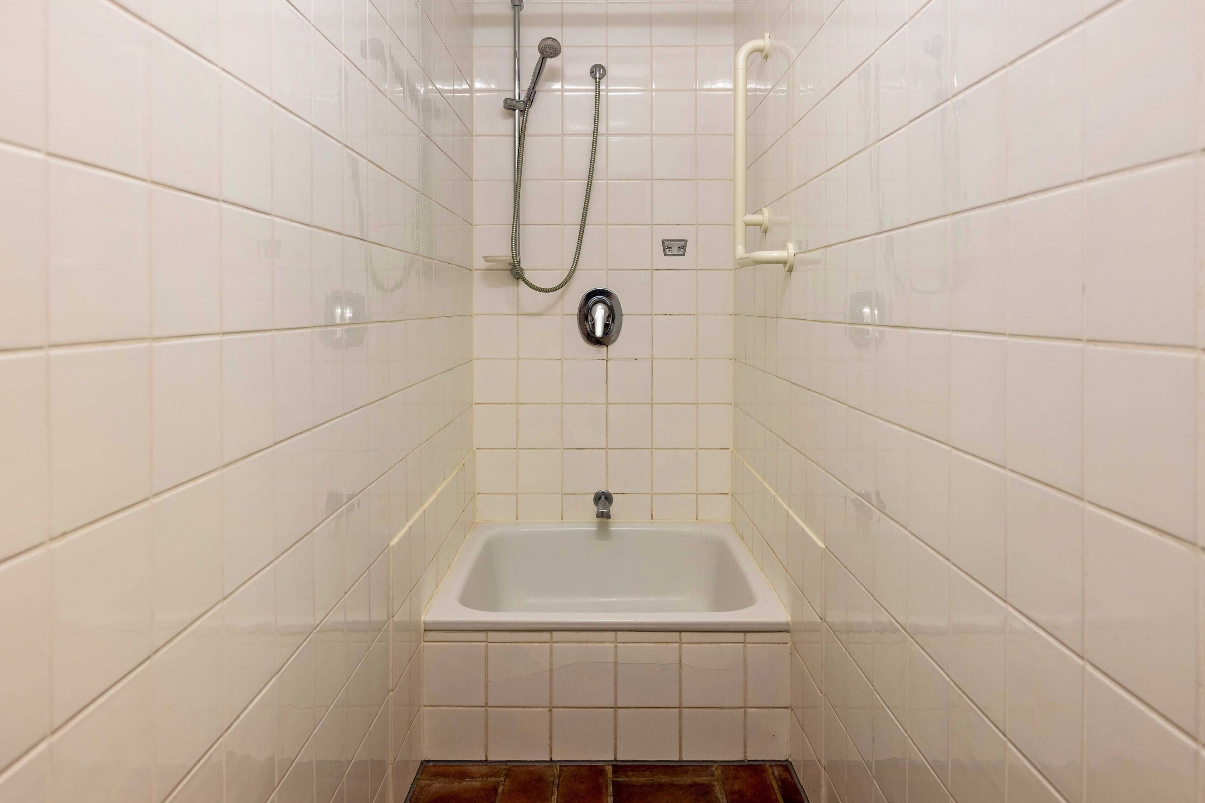 Ein Badezimmer mit weißen Fliesen, einer weißen Badewanne und einer Dusche mit Duschbrause.