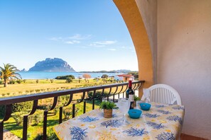 A balcony with a table set for dining, overlooking a scenic landscape with a body of water and a mountain. - Il Vecchio Faro Dalia 6 50m From The Sea, Porto San Paolo, Italy (Porto San Paolo)