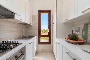 A narrow kitchen with white cabinets, a gas stove, and a window with a view of greenery. - Il Vecchio Faro Dalia 6 50m From The Sea, Porto San Paolo, Italy (Porto San Paolo)