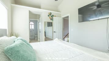 A bedroom with a large bed, a TV mounted on the wall, and a door leading to another room.