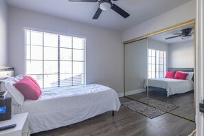 A bedroom with a bed, a ceiling fan, a large window, and a mirror.