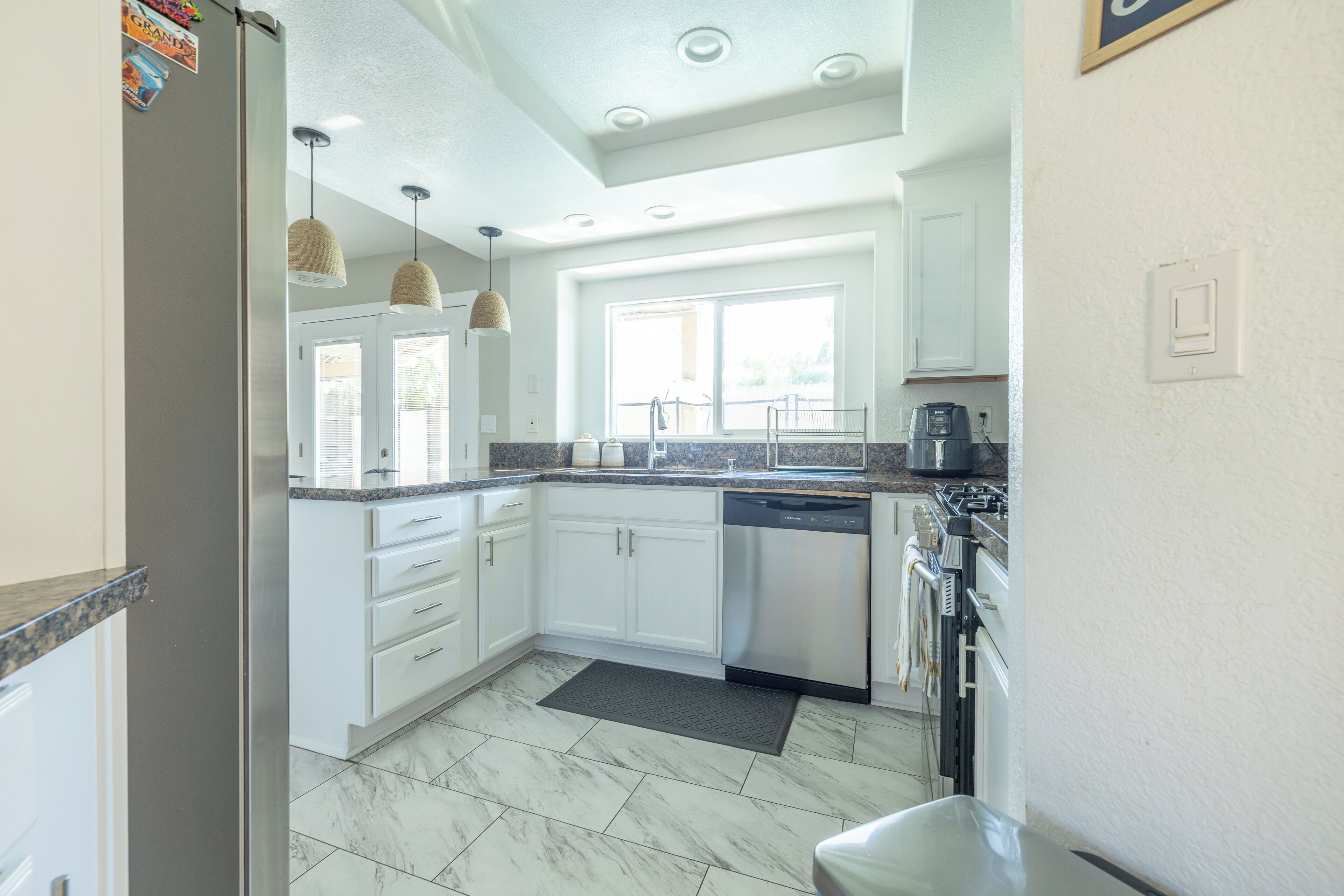 A modern kitchen with white cabinets, a stainless steel dishwasher, and pendant lights.