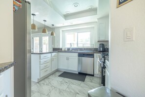 A modern kitchen with white cabinets, a stainless steel dishwasher, and pendant lights. - Family Oasis: Pool & Spa! (Moreno Valley)