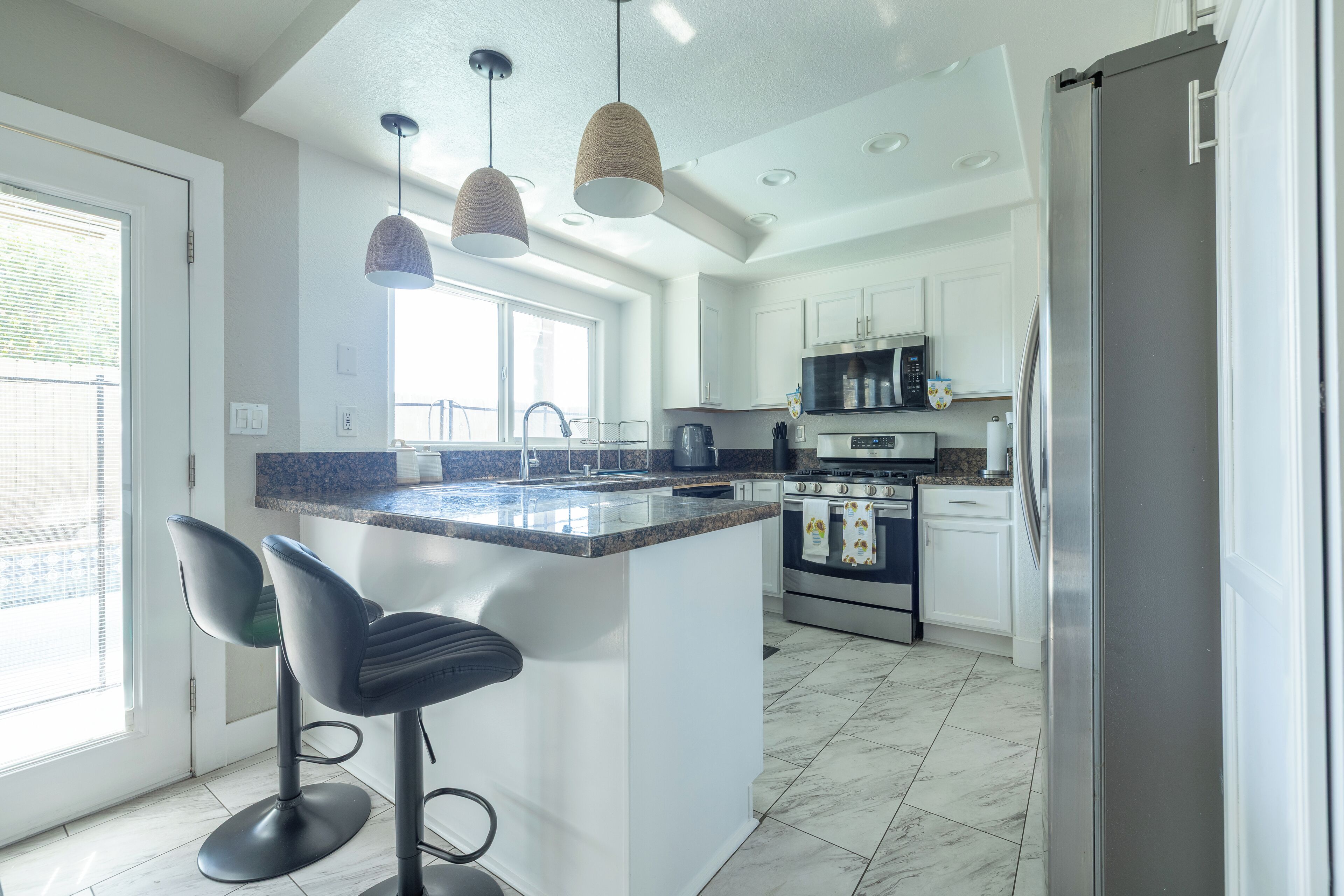 A modern kitchen with a central island, bar stools, pendant lighting, and stainless steel appliances.