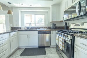 A modern kitchen with white cabinets, a stainless steel dishwasher, a gas stove, and a coffee maker.