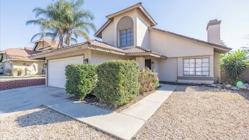 A single-story house with a garage, a small front yard with a palm tree, and a gravel driveway.
