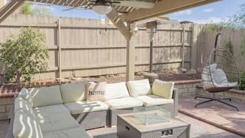 An outdoor patio with a wicker sofa, a glass-top coffee table, and a hanging chair.