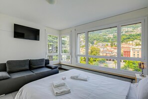Een moderne hotelkamer met een bed, een bank, grote ramen en een flatscreen televisie.