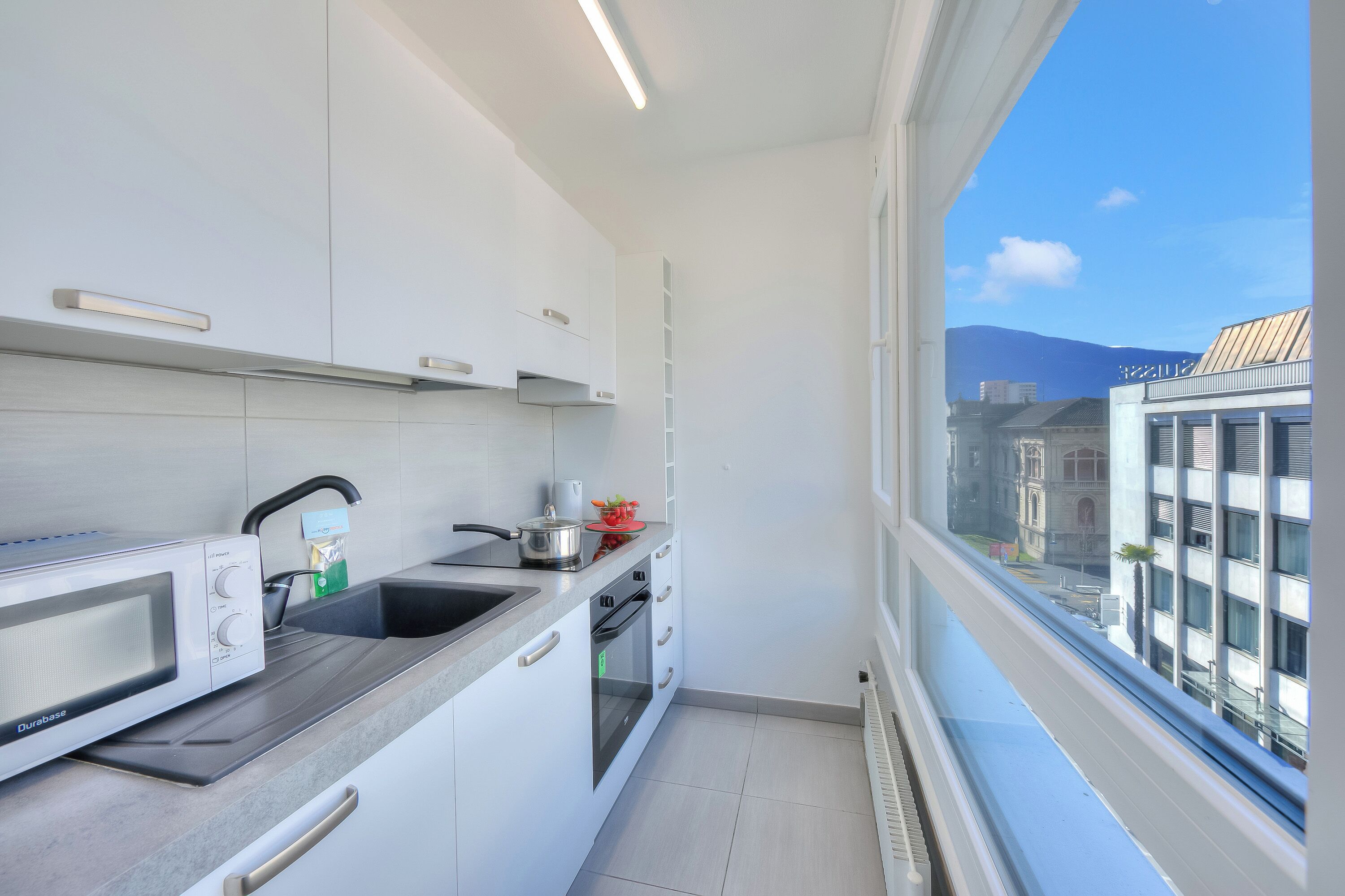 Una cocina moderna con armarios blancos, un microondas, un fregadero y una ventana con vistas a la ciudad.