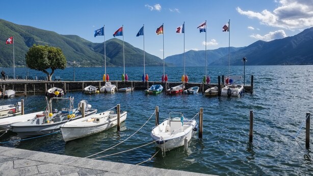 A marina with boats docked, a dock with people, and mountains in the background. - Casa Cupido Locarno Walk to Lake & Centre, Locarno, Switzerland (Locarno)