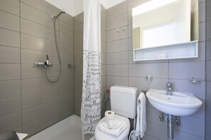 Een badkamer met douche, toilet, wastafel en spiegel.