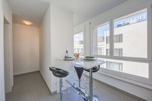Een moderne keuken met een wit aanrecht, twee barkrukken en een raam met uitzicht op gebouwen.